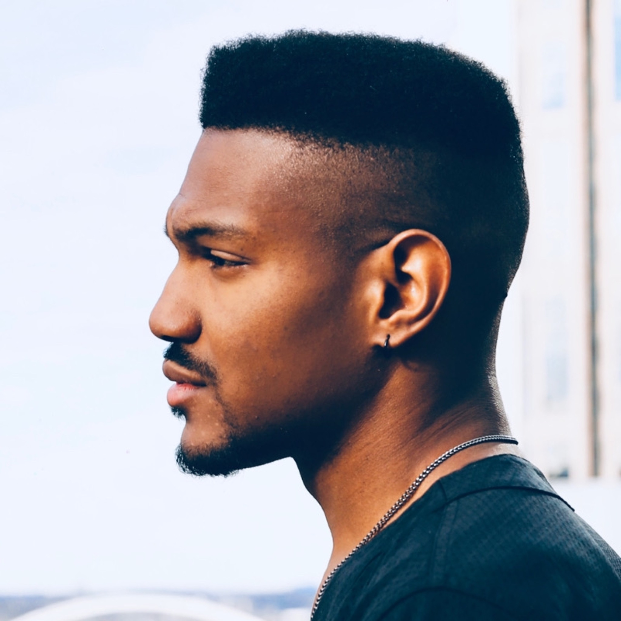 DJ THÄDX in profile, wearing a black shirt and silver chain